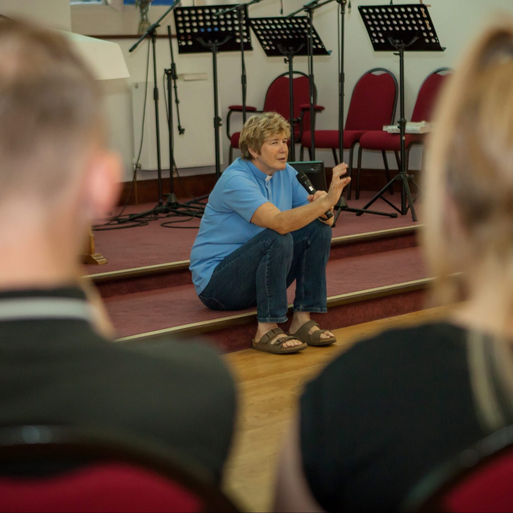 Tracy sat on a step with a microphone talking to a room of young people